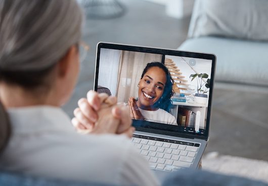 Healthcare professional and patient engaging in a virtual therapy session via laptop, both smiling and gesturing as they communicate through video call