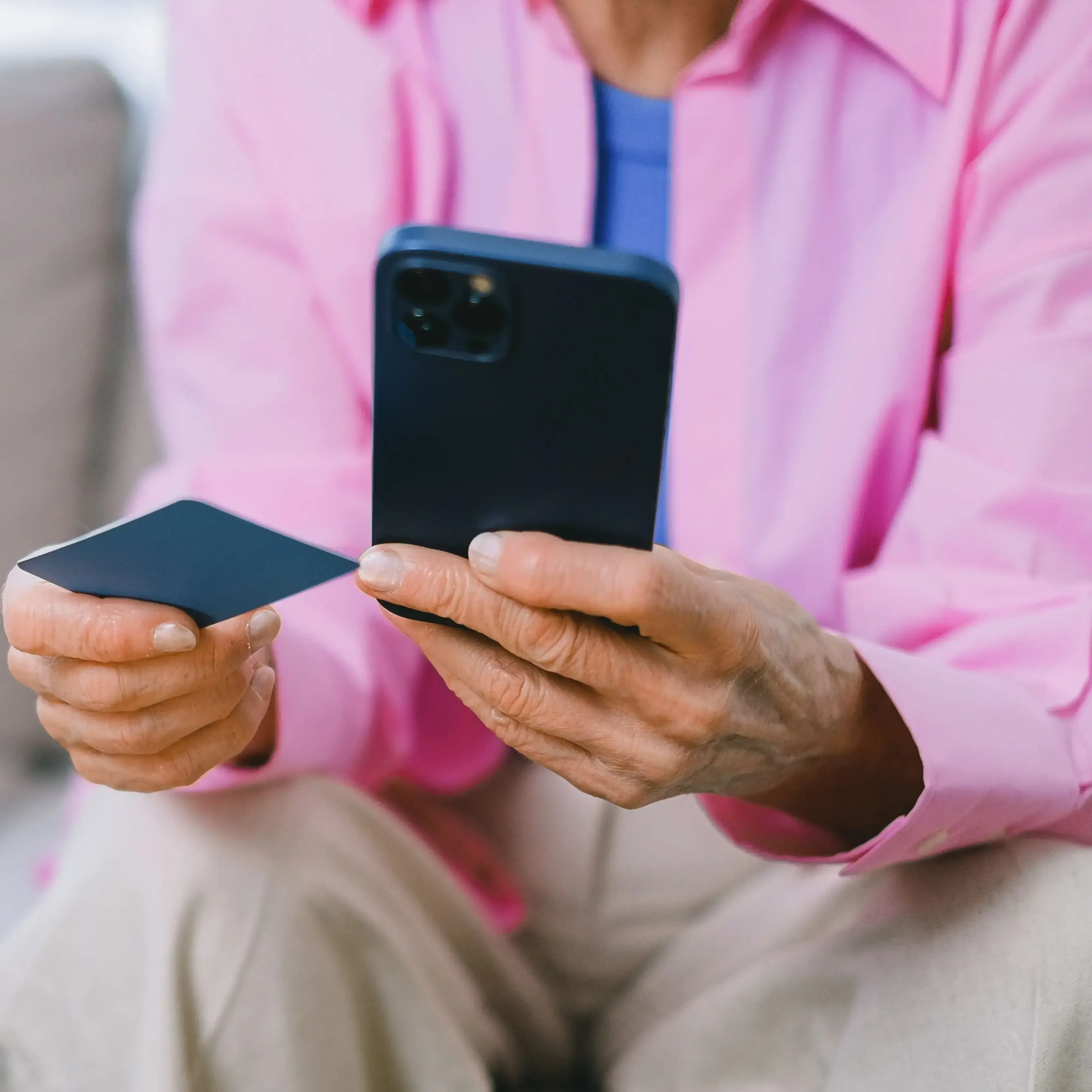 Person in a pink shirt holding a payment card and a phone, paying cash directly for online therapy