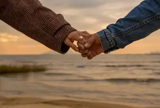 Two people holding hands while walking near a waterfront view.