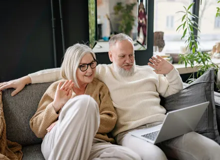 Older couple (man and woman) sitting on a couch meeting with their online couples therapy provider.
