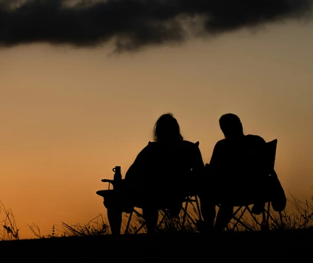 A couple (man and woman) sitting on lawn chairs watching the sunset in front of them