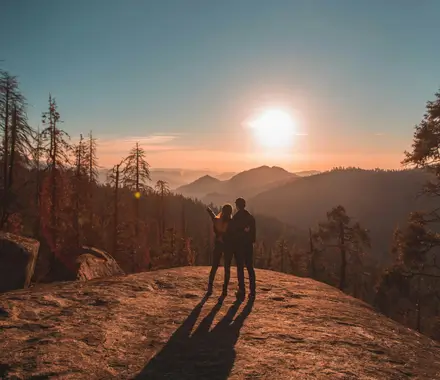 A couple (man and woman) with their arms wrapped around each other staring out at the open mountain range.
