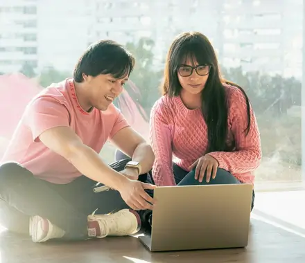 A couple (man and woman) sitting on their apartment floor, using a laptop to research online therapy provider options.