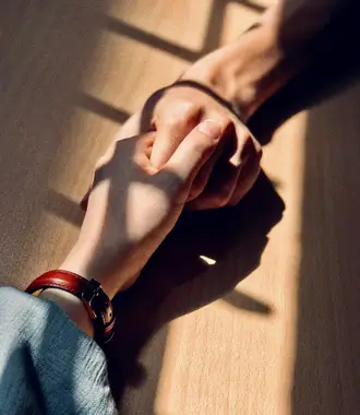 Two people with their hands placed on a table, holding each other's hands.