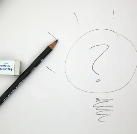 A pencil and eraser sit on top of a piece of paper with a question mark drawn on it.