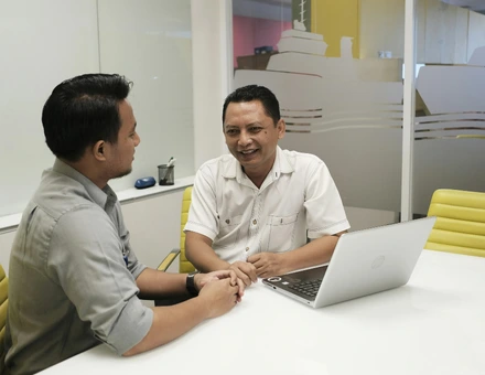Two men sitting at a desk with a laptop open looking for their therapist options.