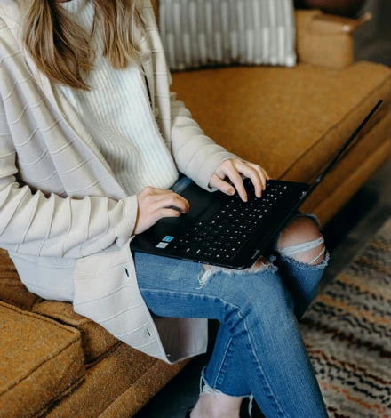 A woman sitting on a couch with her laptop open looking for their therapist options.