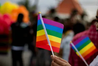 Two miniature pride flags with rainbow colors being waved around by a person