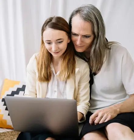 A couple sitting on a couch with their laptop open researching questions about LGBTQIA+ therapy.
