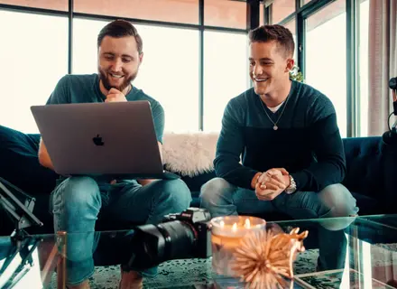 Two men sitting on a couch with their laptop open looking for their therapist options.