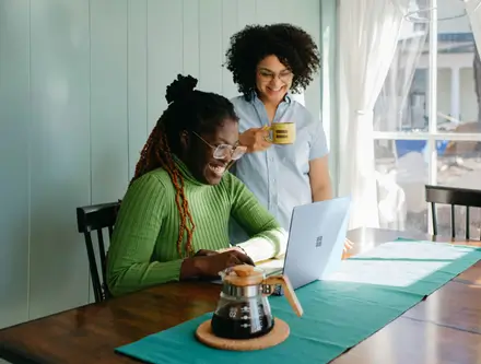 Two women sitting at a coffee table on their laptop looking for their therapist options.