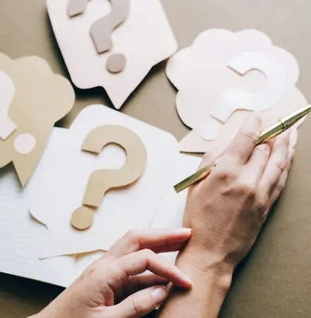 A person sitting at a table with a pen in their hand thinking.