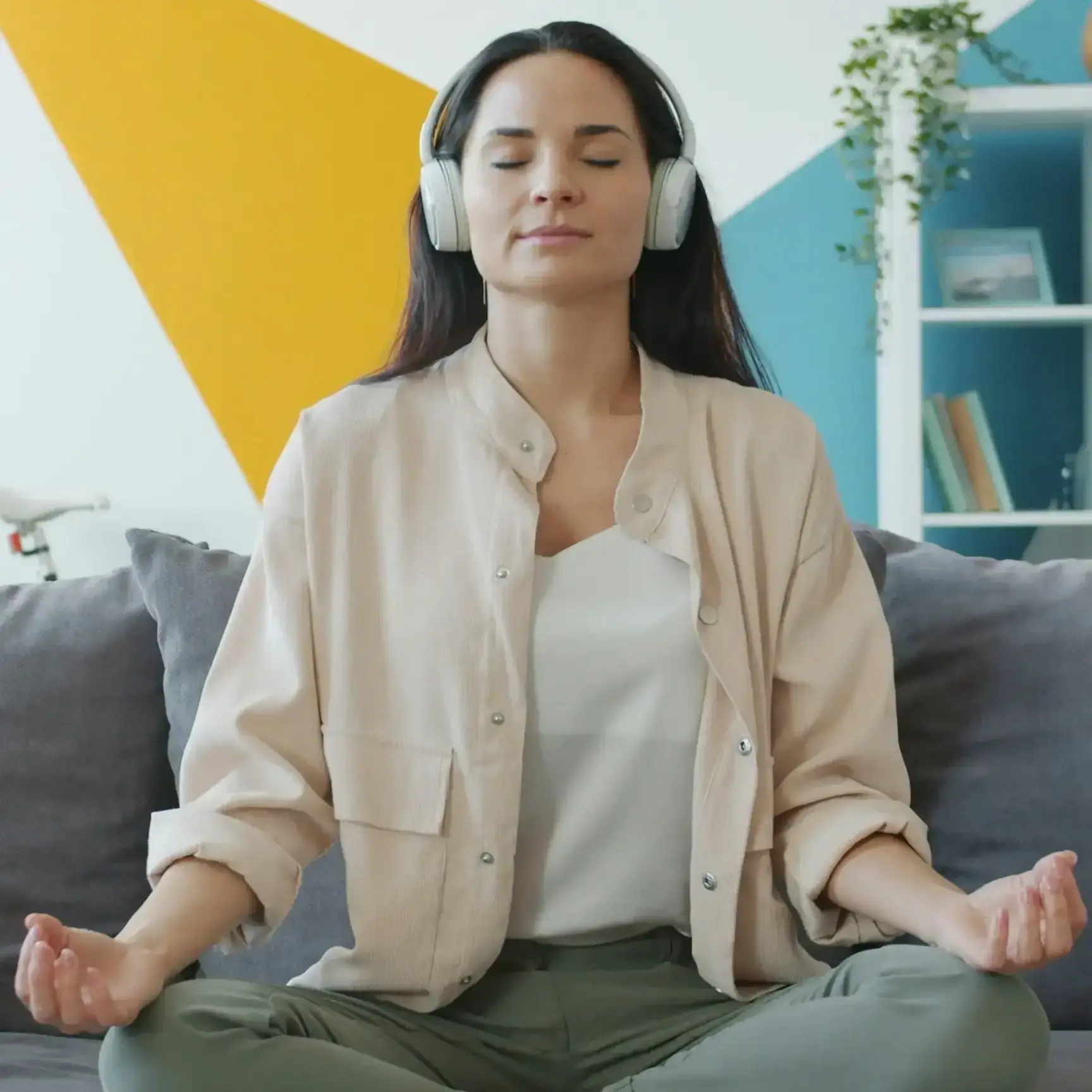A woman wearing headphones meditating cross-legged on a couch at home