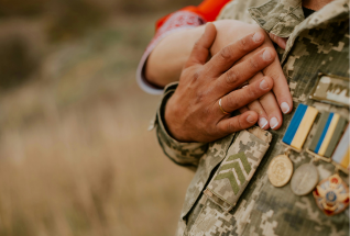 A military solider in uniform embracing his spouse's hand over his chest