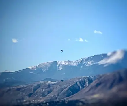 Military solider parachuting with a mountain range in the background.