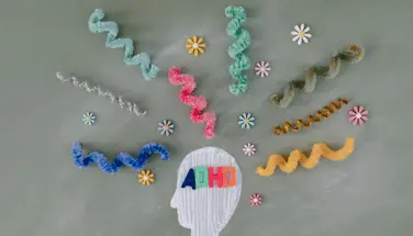 Colorful squiggly yarn or thread pieces radiating outward from central knitted brain shape with scattered decorative elements, representing the scattered attention and hyperactive thought patterns characteristic of ADHD