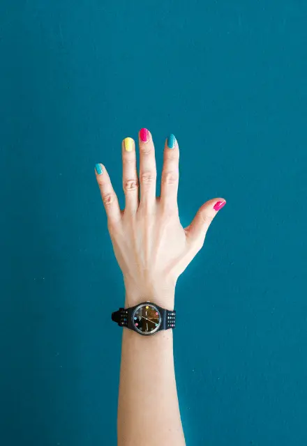 Hand raised against teal background with colorful painted fingernails, symbolizing asking questions or seeking help