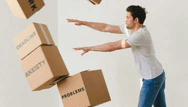 Person with arms outstretched trying to balance falling cardboard boxes labeled with worries, illustrating the overwhelming nature of generalized anxiety and difficulty managing multiple concerns