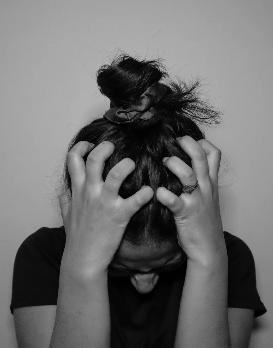 Black and white image of person holding their head in their hands with hair covering face, expressing anxiety and distress