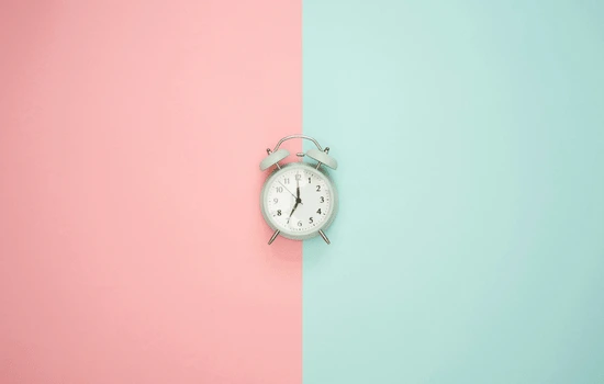 White alarm clock centered on split background of pink and mint green, representing the passage of time during sleepless nights