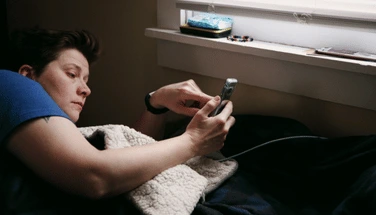 Woman lying awake in bed at day using smartphone, representing sleep difficulties and the struggle to fall asleep associated with insomnia