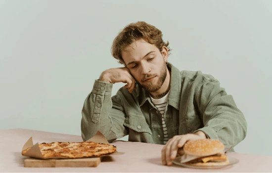 Person sitting at table with multiple plates of food, appearing contemplative or distressed, illustrating compulsive behaviors around eating or food rituals