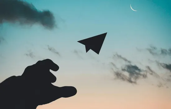 Silhouette of hand releasing or catching a paper airplane against dusky sky with clouds, symbolizing letting go and finding hope after trauma