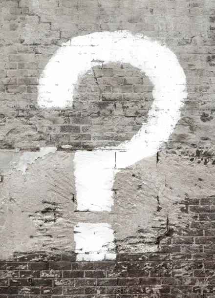 Large white question mark painted on weathered concrete wall next to street sign, representing questions about PTSD therapy and seeking help after trauma