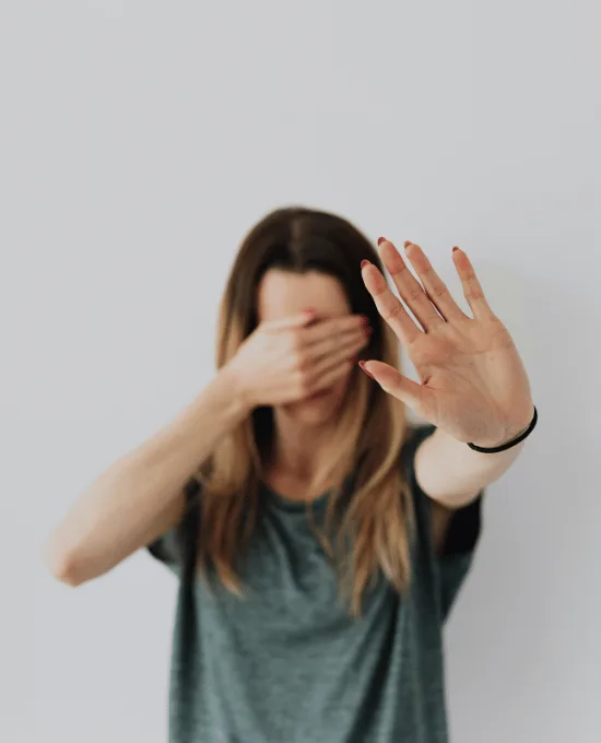 oman holding up her hand in a stop gesture while covering her face with the other hand, illustrating avoidance and protective responses common in PTSD