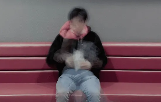 Person sitting alone on red bleacher steps with head down and hood up, illustrating social isolation and withdrawal associated with social anxiety