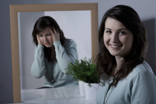 Split reflection showing woman holding her head in distress on one side and smiling calmly on the other, illustrating the contrasting mood episodes of depression and mania in bipolar disorder