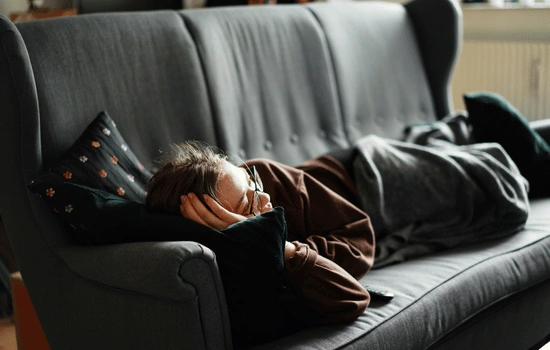 Person lying on dark couch in dim lighting, appearing exhausted and withdrawn, illustrating the persistent fatigue and hopelessness of treatment-resistant depression